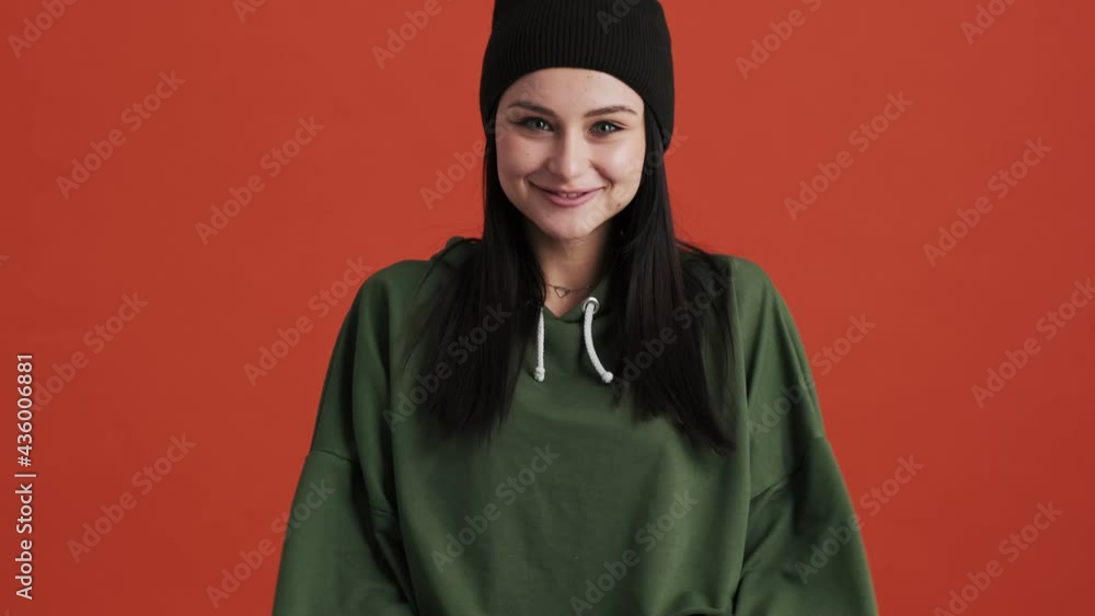 A surprised woman wearing hoodie is looking to the camera standing isolated over red wall in the studio A surprised woman wearing hoodie is looking to the camera standing isolated over red wall in the studio