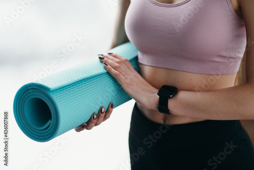 Close-up photo. Girl in a sports top and leggings in the gym holds a yoga mat in her hand