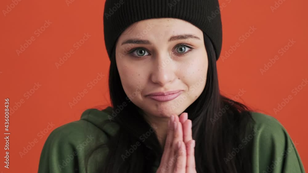 A close-up view of a cute woman is asking for something holding hands in a praying gesture standing isolated over red wall in the studio A close-up view of a cute woman is asking for something holding hands in a praying gesture standing isolated over red wall in the studio