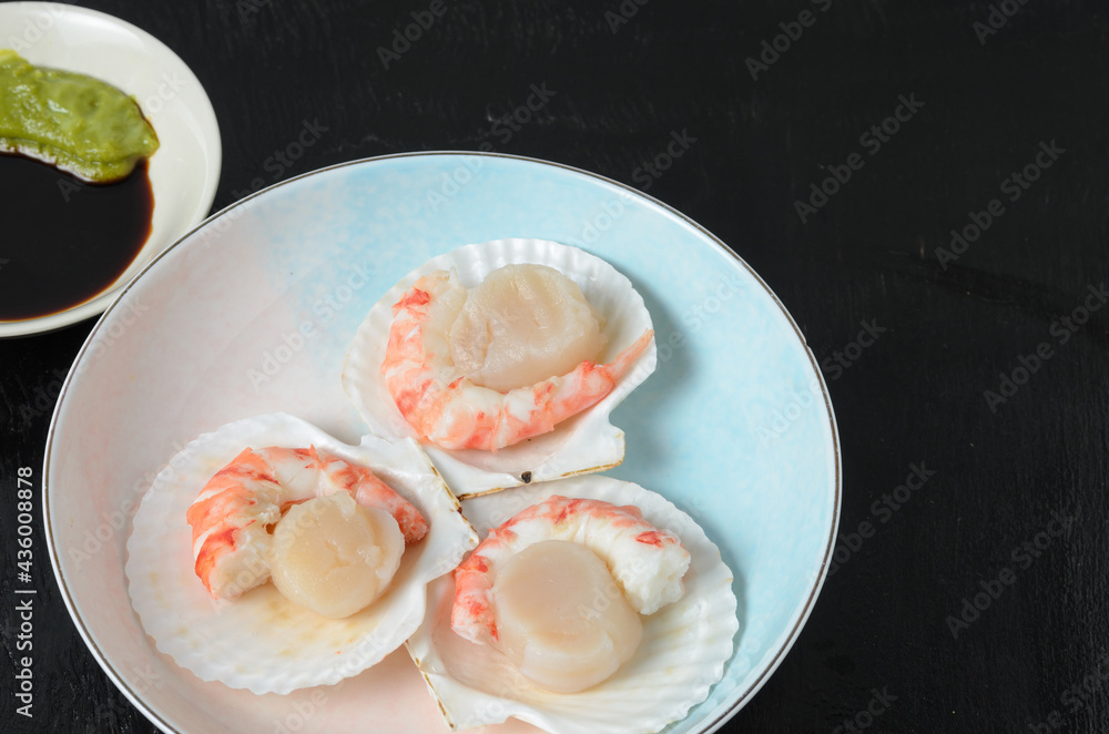 Natural raw scallop with boiled shrimp in the sink in a ceramic bowl with soy sauce and wasabi on a dark background. Natural raw scallop with boiled shrimp in the sink in a ceramic bowl with soy sauce and wasabi on a dark background.