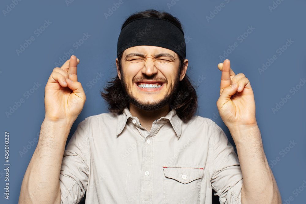 Studio portrait of excited young man with crossed fingers on blue background. Studio portrait of excited young man with crossed fingers on blue background.