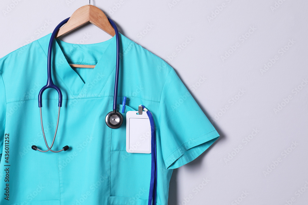Turquoise doctor shirt with stethoscope, badge and pen hanging on light grey background. Space for text Turquoise doctor shirt with stethoscope, badge and pen hanging on light grey background. Space for text