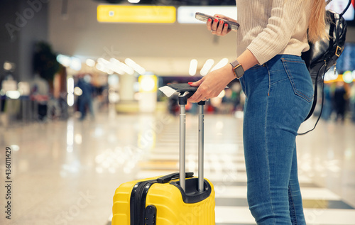 Young woman holding phone and yellow suitcase luggage with passport and plane ticket at airport