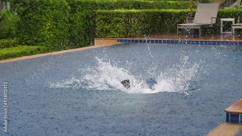 Adult woman clumsily jump in swimming pool, create big splash of water. Slow motion shot of tourist have fun at rainy day, fall plop in pool, heavy tropical rain pouring down