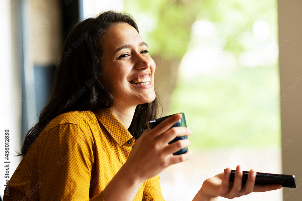 Young businesswoman drinking coffee in her office. Beautiful smiling woman enjoying in a cup of coffee.