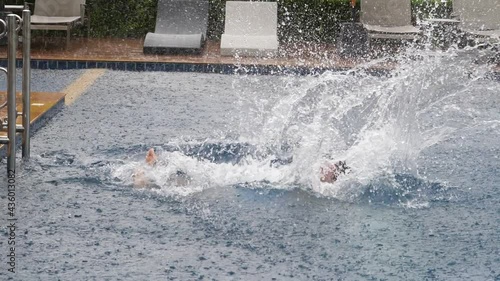 Man fall into water of swimming pool, clumsy swing hands and plop flat on back with big splash, slow motion shot. Heavy tropical shower, typical weather at Thailand in rainy season