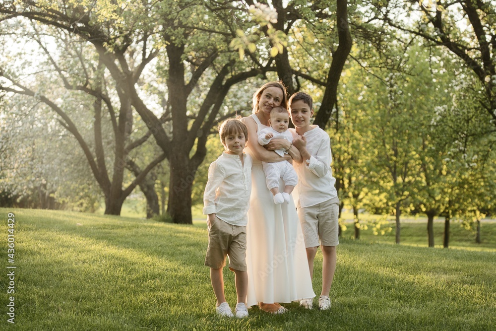 Mother and three children hugging. Happy family sitting outdoor: woman and two brother kids boys and cute little toddler boy Mother and three children hugging. Happy family sitting outdoor: woman and two brother kids boys and cute little toddler boy