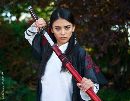 Young asian girl in traditional kimano in a blooming garden with samurai japanese sword katana in image of warrior woman photo