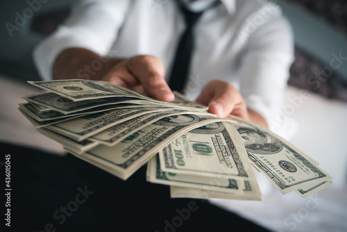 Selective focus. Close up of businessman hand offering batch of hundred dollar bills.Venality, bribe, corruption concept.