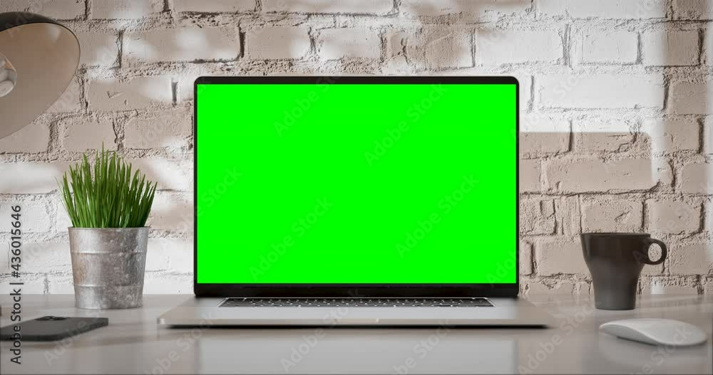 Laptop green screen is opening. Loft office interior with brick wall and swaying trees on the wind. The last 200 frames are looped