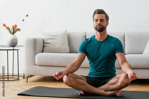 man with closed eyes meditating in lotus pose on yoga mat
