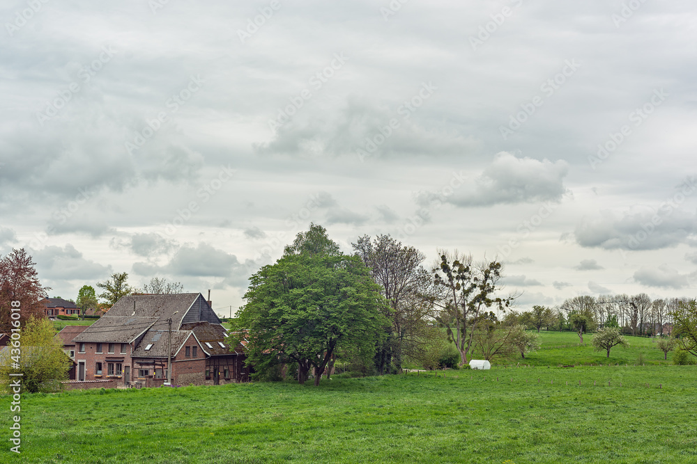 Obraz premium Old farmhouse in a green hilly spring landscape with a cloudy sky.