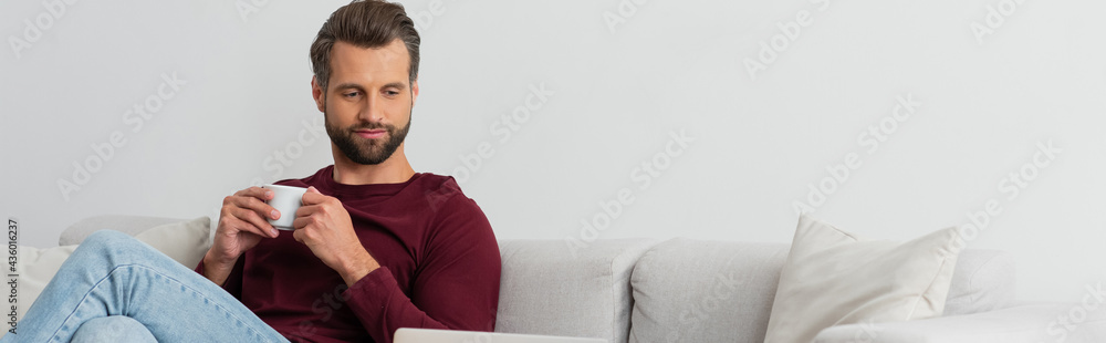 smiling man sitting on couch with cup of coffee, banner