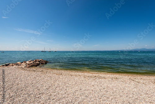 Fototapeta Naklejka Na Ścianę i Meble -  Beautiful beach on Lake Garda (Lago di Garda) between the small villages of Cisano and Bardolino. Verona province, Veneto, Italy, southern Europe. Lombardy coast on the horizon.