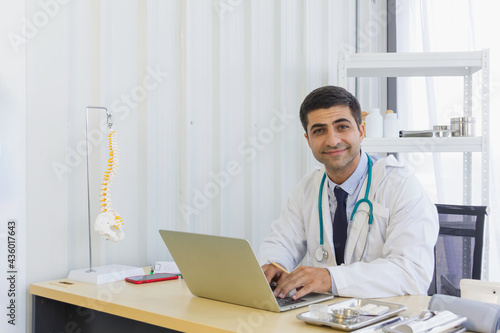 male doctor sitting in front of a computer in a clinic with a simulated spinal structure