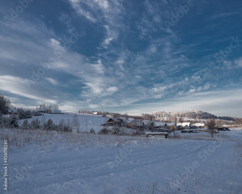 Snow-covered village at the hill on a frosty winter day. Beautiful landscape with village and conifer forest on snowy day.