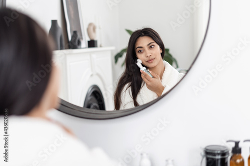 Young asian female using silicone face brush in front of mirror