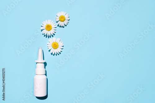 Nasal spray and natural chamomiles on a blue background. Treating seasonal allergies. Top view, place for text.