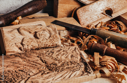 Photo of wooden old fashioned planes with carving chisels laying on workbench table with dragon and woman goddess bas -relief wooden sculpture.