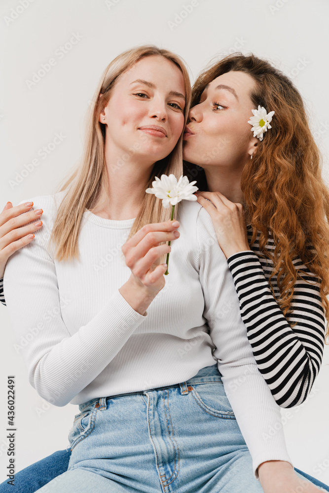 Young white two women kissing while hugging and posing with flowers Young white two women kissing while hugging and posing with flowers