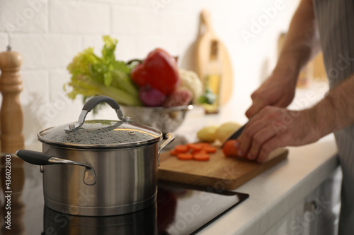 Homemade bouillon recipe. Man cutting carrot in kitchen, focus on pot