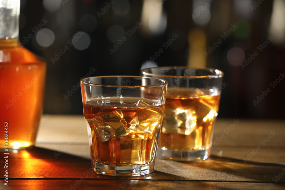 Glasses of whiskey with ice on wooden table in bar, space for text Glasses of whiskey with ice on wooden table in bar, space for text