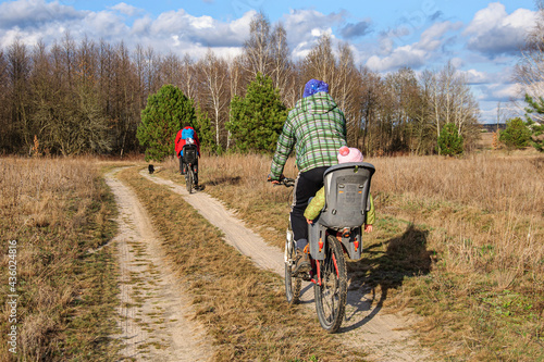 Dads ride their daughters on bicycles in bicycle seats on a dirt road through the forest