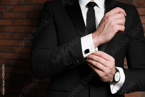 Man wearing stylish suit and cufflinks near brick wall, closeup