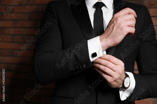 Man wearing stylish suit and cufflinks near brick wall, closeup photo