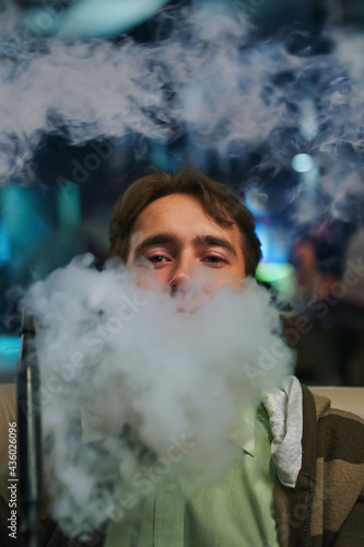 Portrait of a young man in the smoke. Man in restaurant smoking hookah. Person on sofa in cafe. Relax on shisha bar.