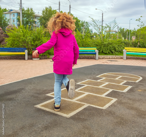 Redhead girl playing hopscotch on school playground. Back view. No faces.