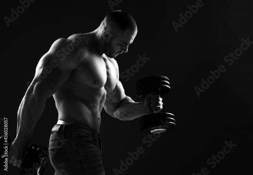 Silhouette of Brutal strong man athlete in jeans doing workout with dumbbel showing pumped up sexy body and biceps over dark background, side view. Sport men body concept