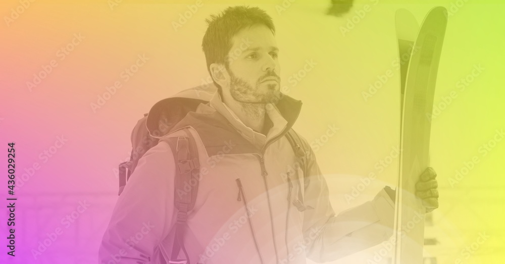 Composition of male skier holding skis in mountains with pink to green tint Composition of male skier holding skis in mountains with pink to green tint