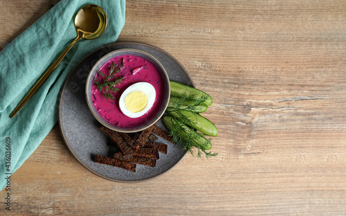 cold soup with kefir and beetroot in a gray plate with bread croutons and cucumbers on a wooden background with celery leaves on the left. Place for text