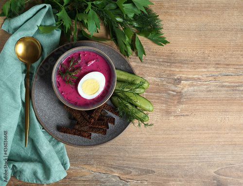 cold soup with kefir and beetroot in a gray plate with bread croutons and cucumbers on a wooden background with celery leaves on the left corner and golden spoon. place for text
