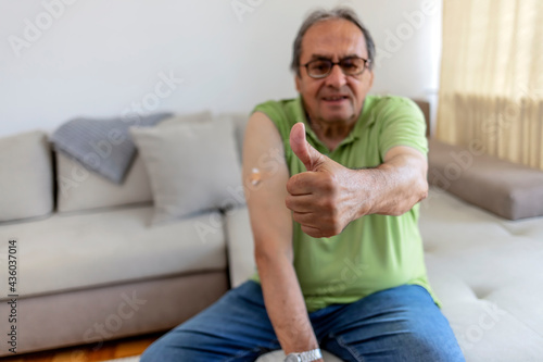 Selective focus of a senior man that has received his first dose of COVID-19 vaccine. Man is pulling up his sleeve to show bandage from vaccination. Man pointing his shoulder after getting vaccinated. © Jelena Stanojkovic