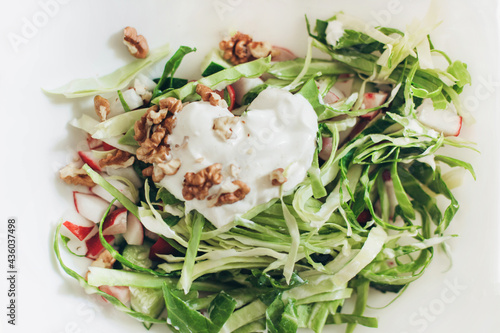 Summer vegetable salad. Heart Shaped Sour Cream. Fresh cabbage radishes, walnuts, chopped on a white background 