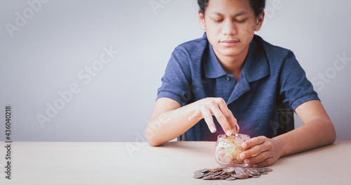 Save money concept, teenager boy hands holding coins stack glass jar, young boy looking stack coins conceptual save money for future,  design idea saving money copy space background.