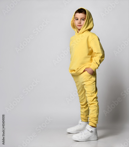 Stylish boy in yellow sportswear, white sneakers. Playful child on a gray background. School student is ready for a sports lesson. photo