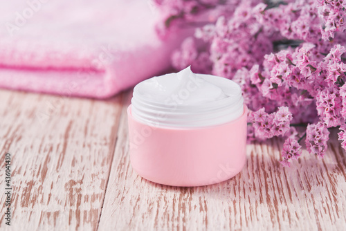 Hygienic cream skincare product  in pink plastic jar with towel on white table.