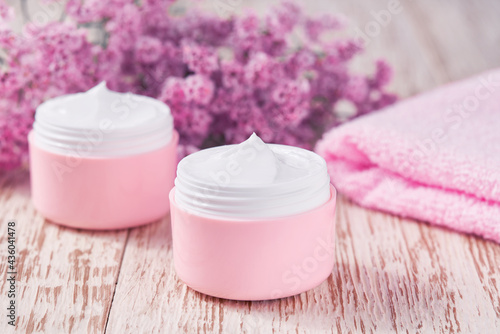 Natural face cream or lotion  organic cosmetic product to moisturize the skin with a towel and flowers on the background. Pink series  cosmetic.