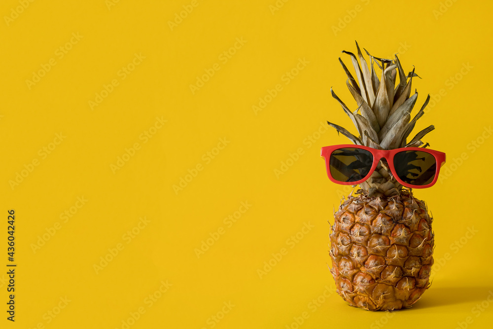 Ripe fresh pineapple with sunglasses isolated on yellow background. The concept of a hot summer, rest and vacation
