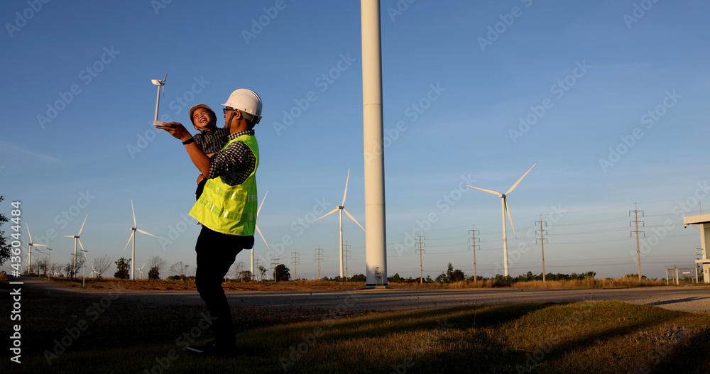 Asian father engineer enjoying and holding son in the wind turbines farm, Family with environmental engineering renewable energy concept