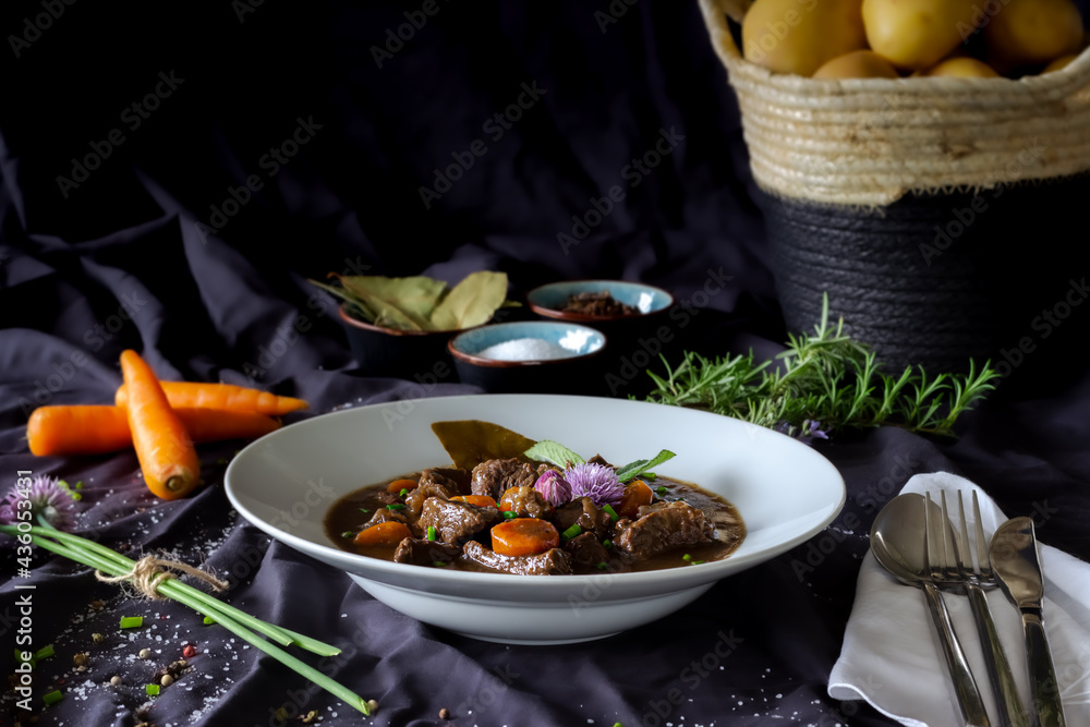 beef ragout stew with carrots, vegetables and greens on black background