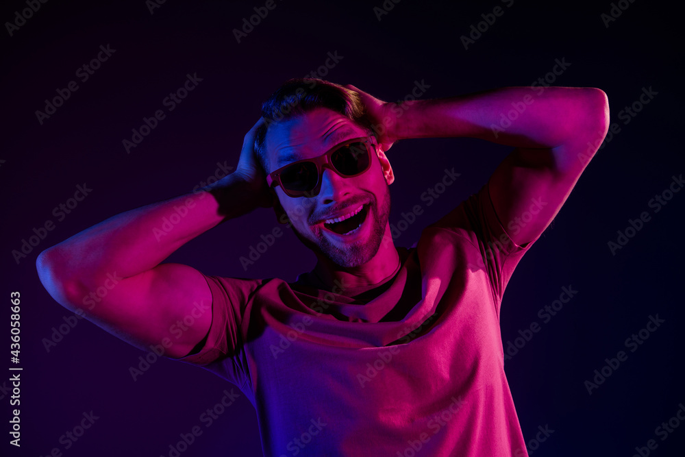 Portrait of attractive cheerful funny guy touching hair having fun isolated over dark neon violet color background Portrait of attractive cheerful funny guy touching hair having fun isolated over dark neon violet color background