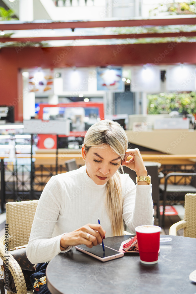 Vertical shot of a blonde Hispanic female using her phone in a cafe Vertical shot of a blonde Hispanic female using her phone in a cafe