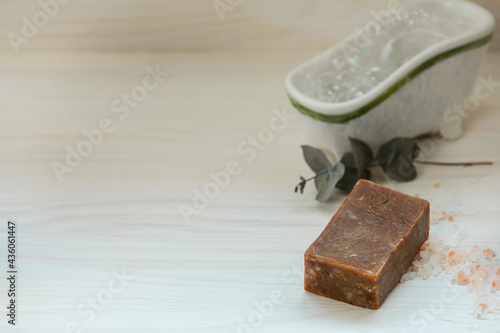 Fototapeta Naklejka Na Ścianę i Meble -  Organic brown soap with mini bathtub on light natural wooden background with a branch of eucalyptus. The concept of Self-care. Copy sapce.