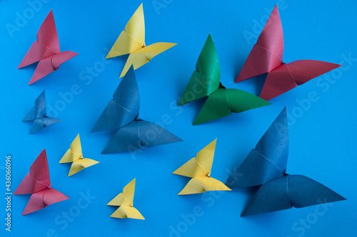 multicolored origami paper butterflies of different sizes on a blue paper background