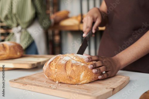 Close-up of woman cutting baked fresh bread in the bakery