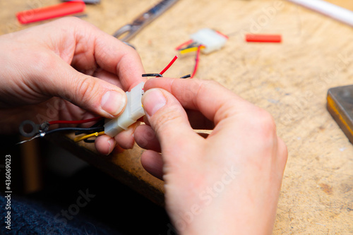 Young man s hands hold multicolored wires over desk with tools